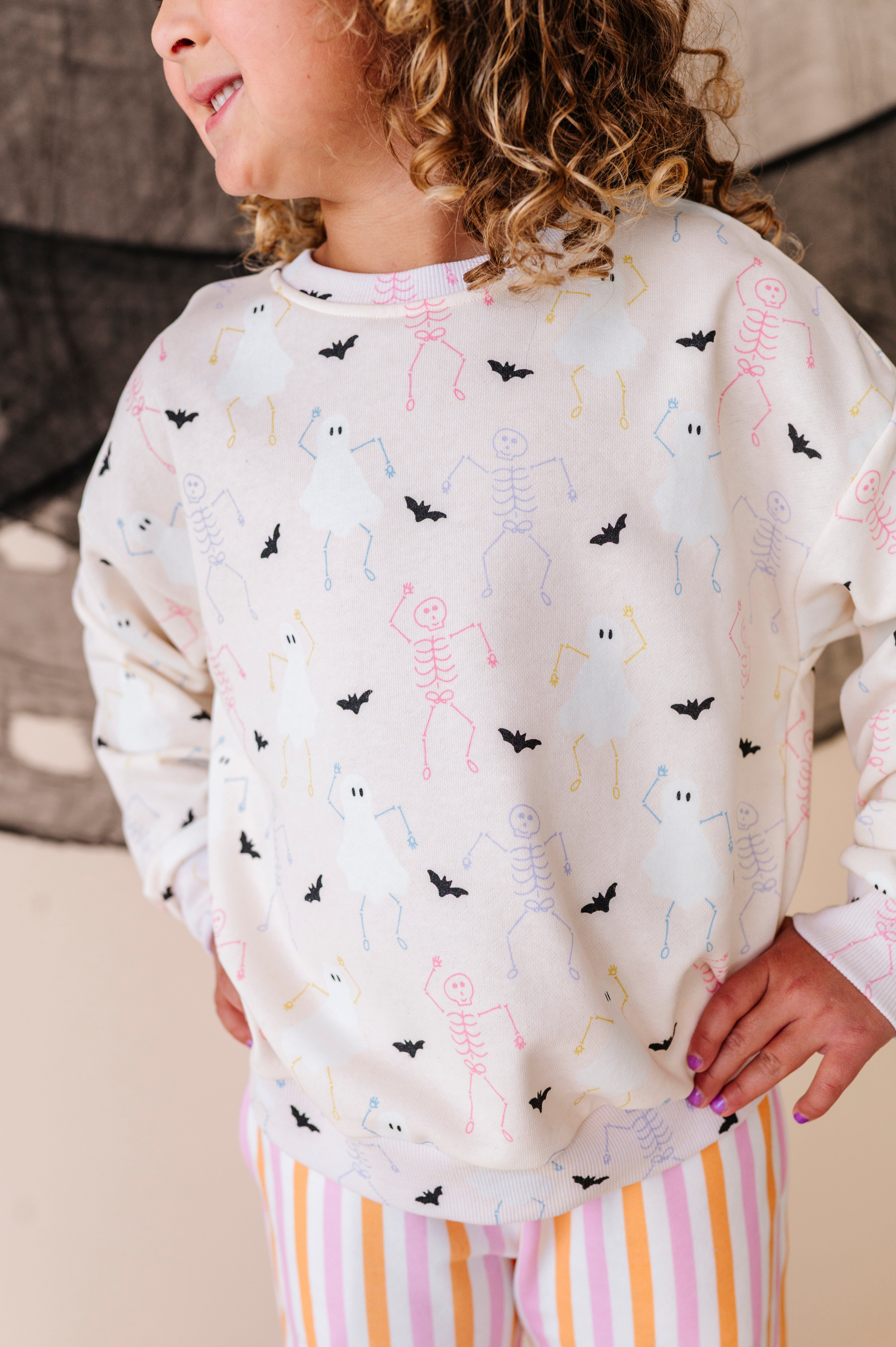 Child wearing a sweatshirt set with skeleton, ghost, and bat pattern